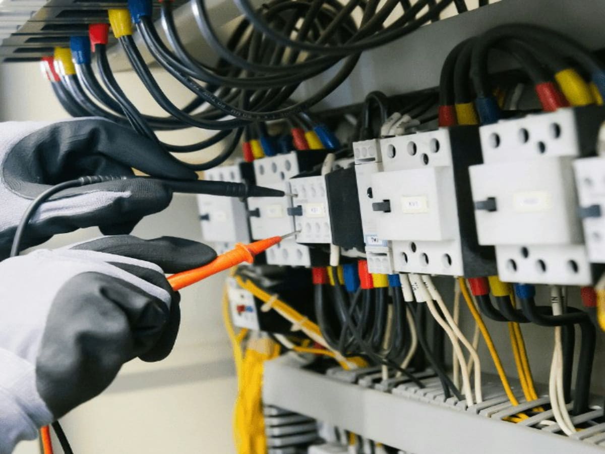 Électricien vérifiant les contacteurs d'un tableau électrique professionnel au multimètre